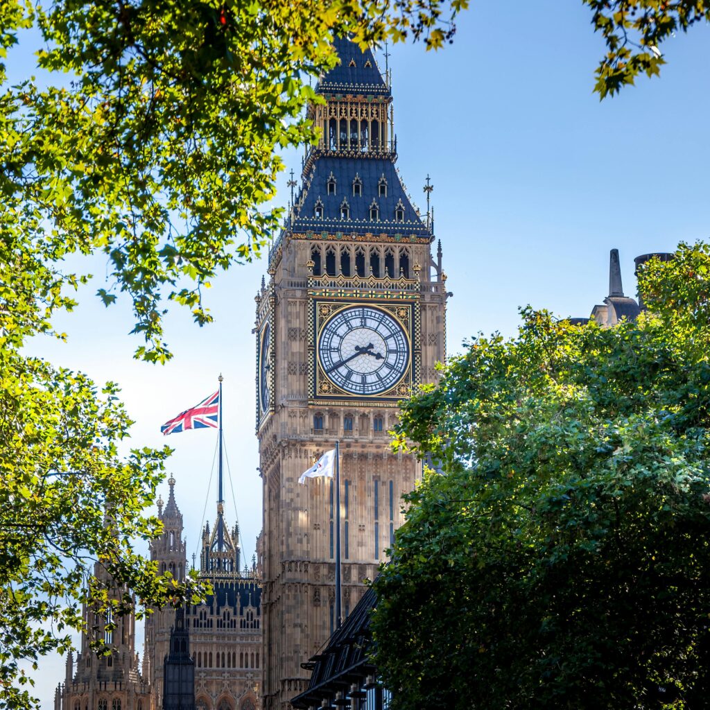 Stunning view of Big Ben and Union Jack against the clear blue sky, framed by lush trees.